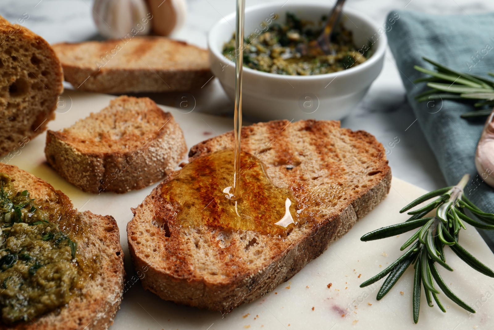 Photo of Pouring oil onto slice of toasted bread on board, closeup