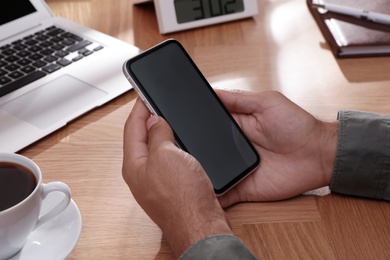 Man holding mobile phone with empty screen at table, closeup