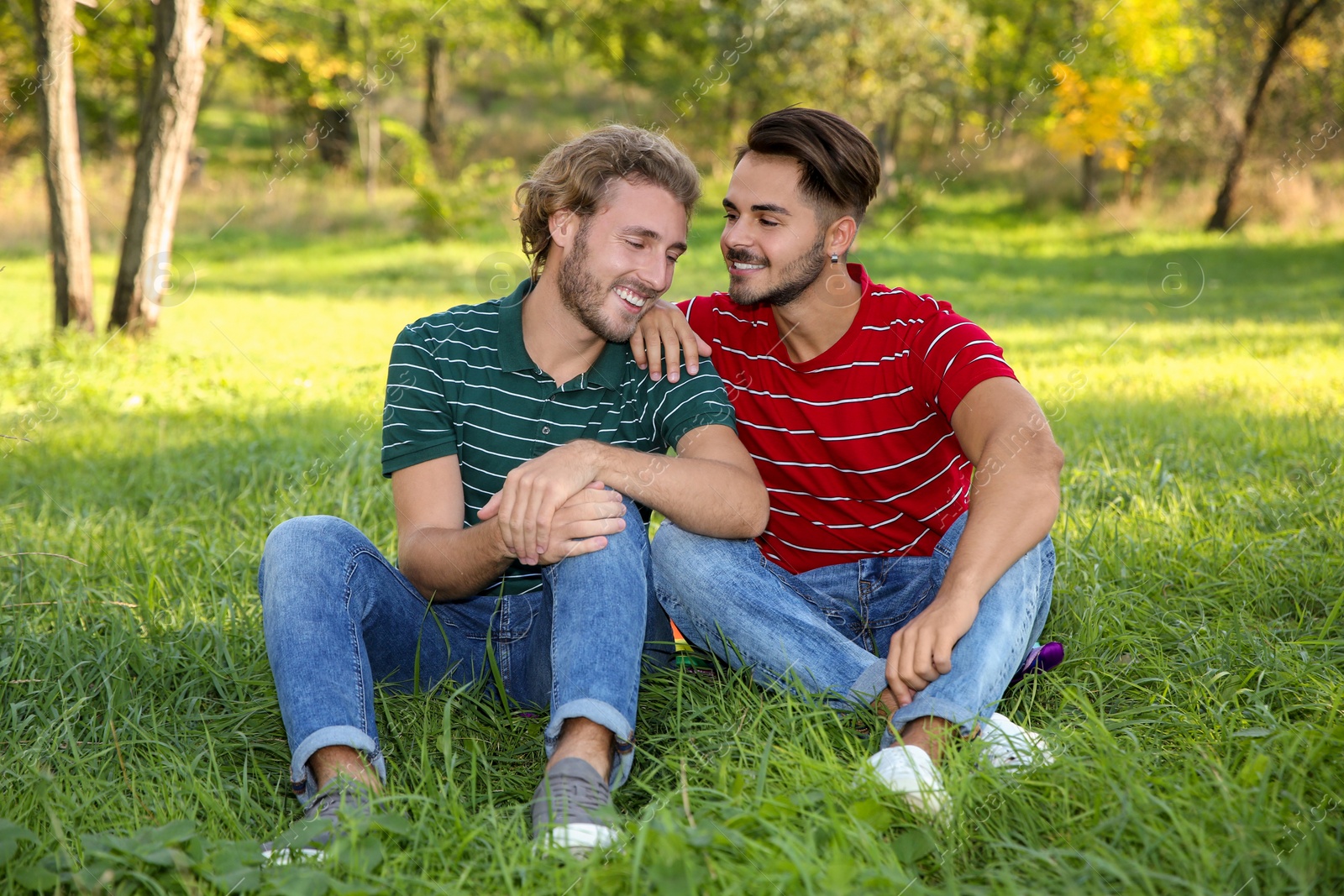 Photo of Portrait of happy gay couple sitting on grass in park