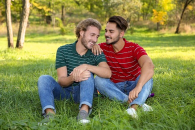 Portrait of happy gay couple sitting on grass in park