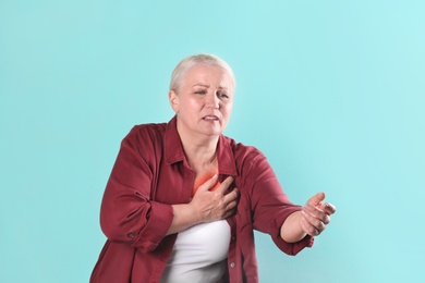 Mature woman having heart attack on color background