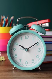 Photo of Alarm clock and different stationery on wooden table near green chalkboard, closeup. School time