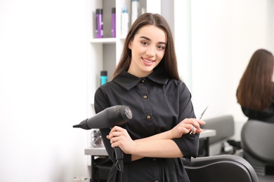 Photo of Professional female hairdresser with dryer and scissors in salon