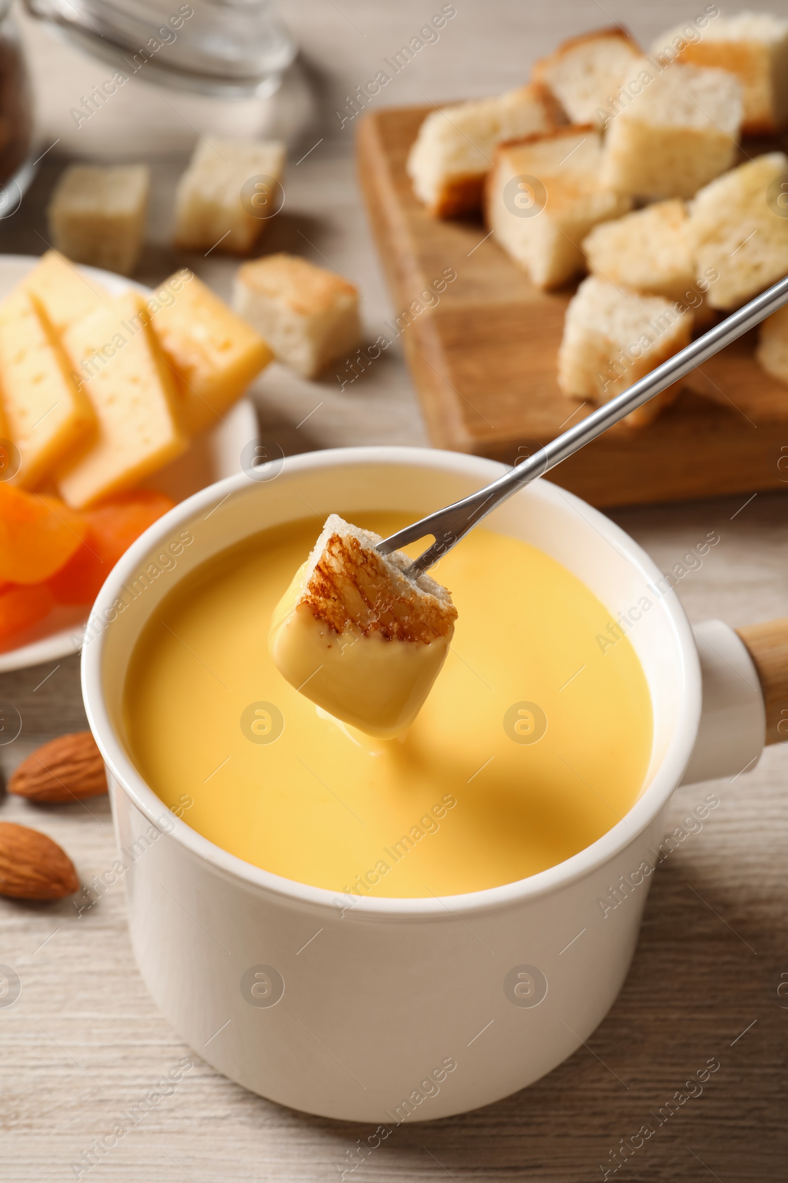 Photo of Dipping piece of bread into tasty cheese fondue on light wooden table