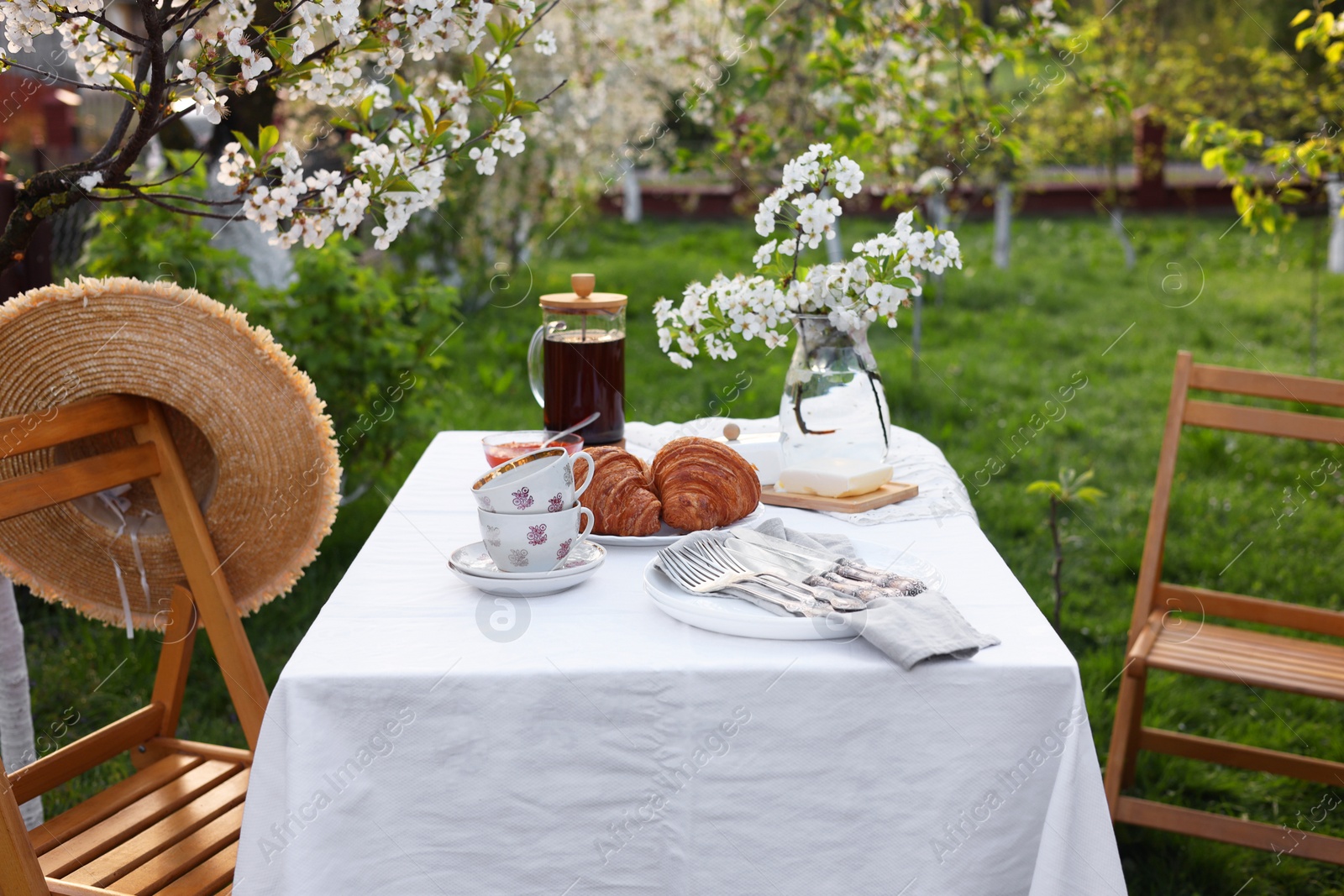 Photo of Stylish table setting with beautiful spring flowers, tea and croissants in garden