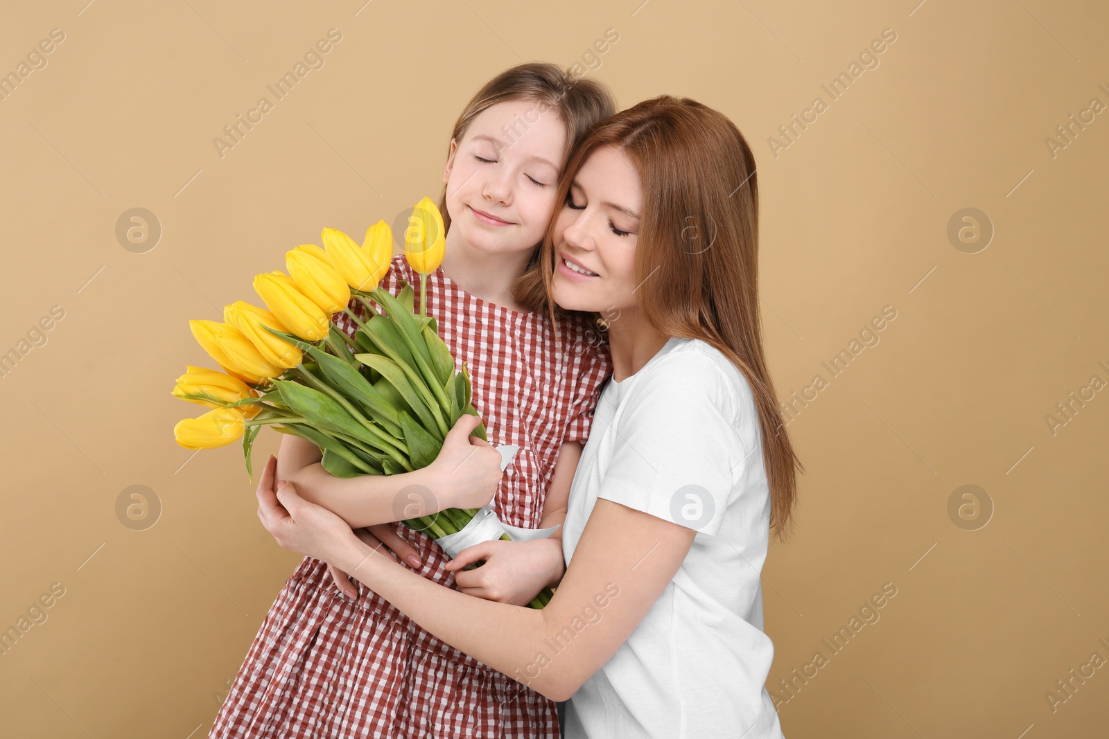 Photo of Mother and her cute daughter with bouquet of yellow tulips on beige background