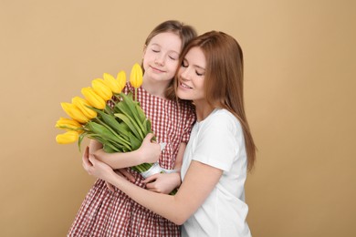Mother and her cute daughter with bouquet of yellow tulips on beige background