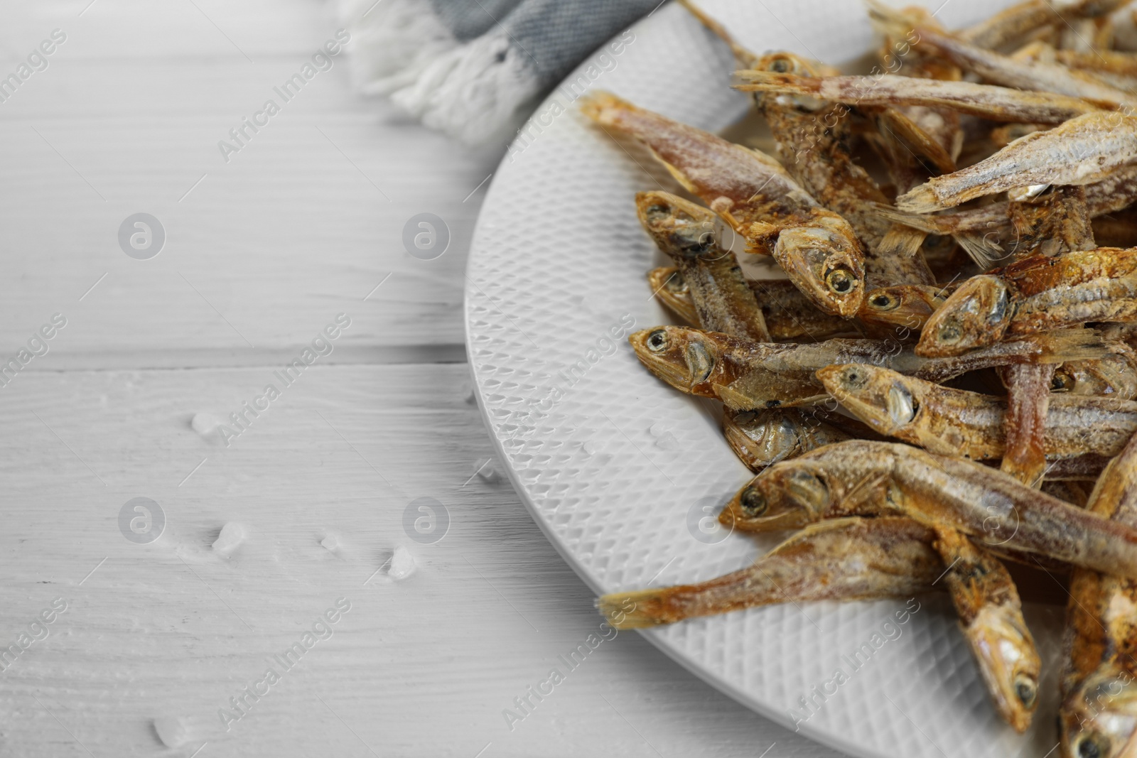 Photo of Plate with tasty dried anchovies on white wooden table, closeup. Space for text