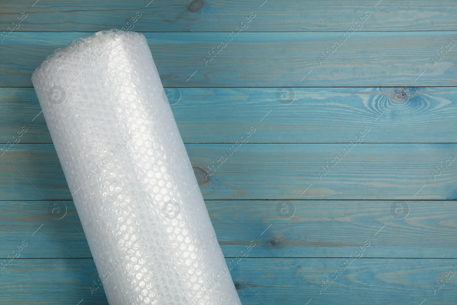 Photo of Bubble wrap roll on light blue wooden background, top view. Space for text