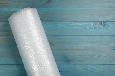 Bubble wrap roll on light blue wooden background, top view. Space for text