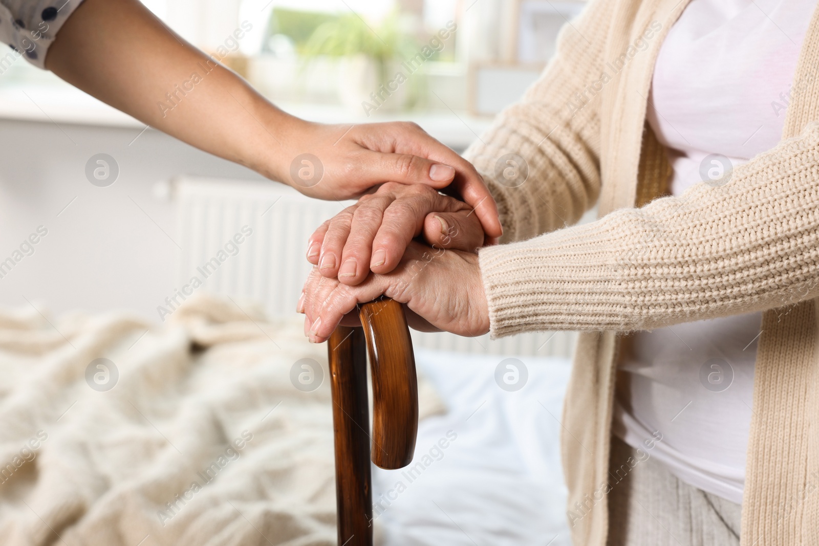 Photo of Caregiver and elderly woman with walking cane at home, closeup