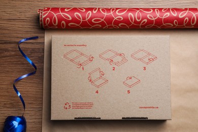 Photo of Roll of wrapping paper, gift box and ribbon on wooden table, flat lay