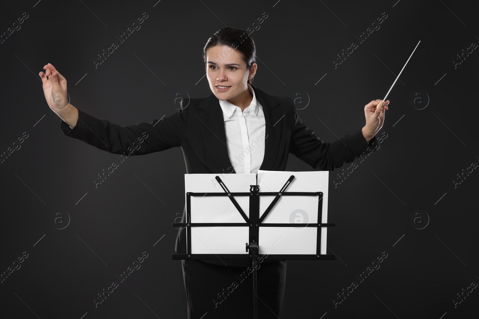 Photo of Happy young conductor with baton and note stand on dark background