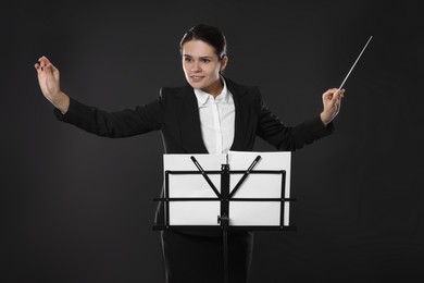 Photo of Happy young conductor with baton and note stand on dark background