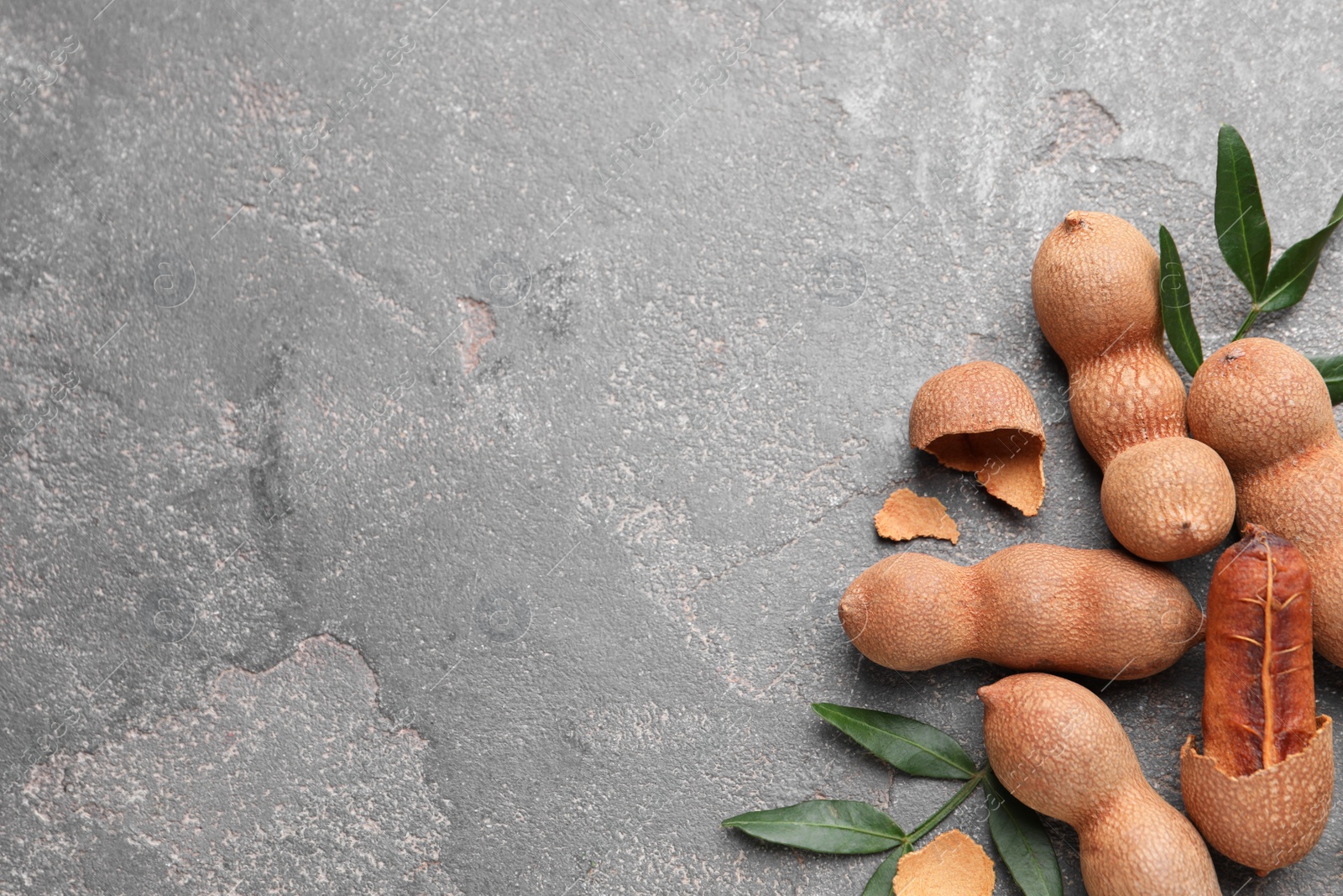 Photo of Ripe tamarinds and fresh leaves on grey table, flat lay. Space for text