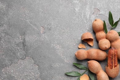 Photo of Ripe tamarinds and fresh leaves on grey table, flat lay. Space for text