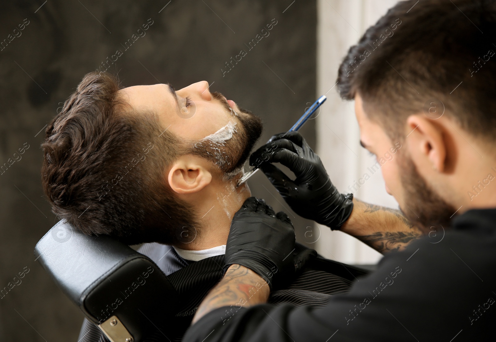 Photo of Professional hairdresser shaving client with straight razor in barbershop