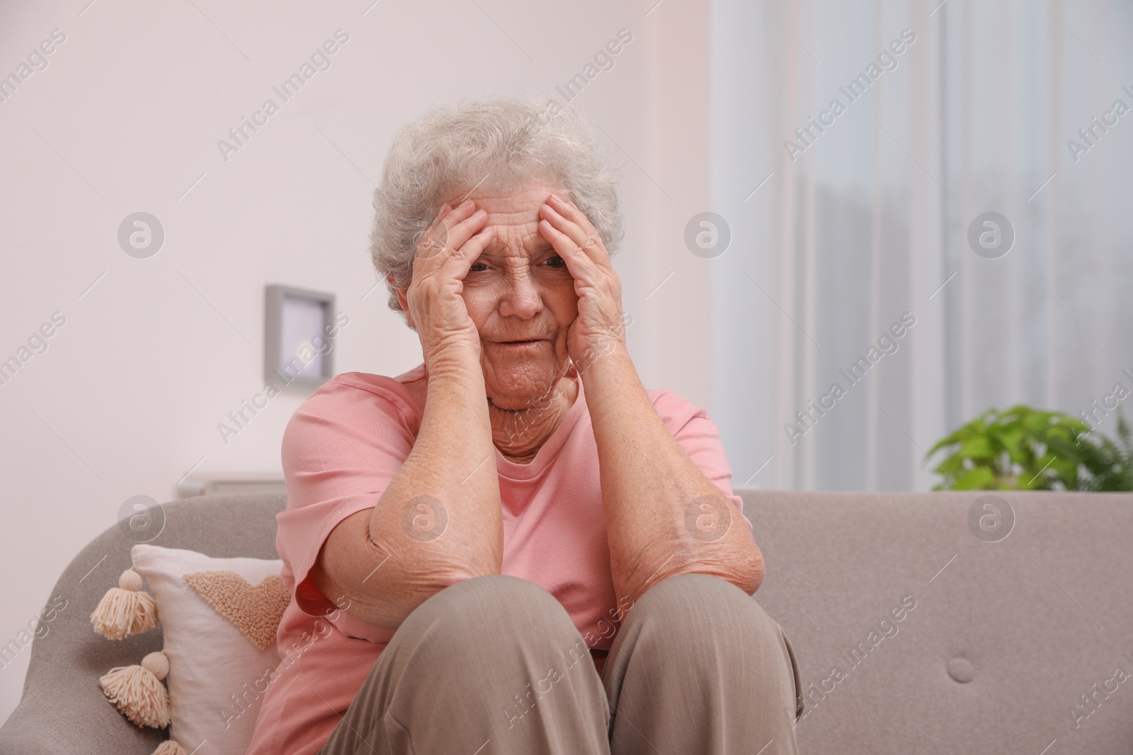 Photo of Senior woman with headache sitting on sofa at home