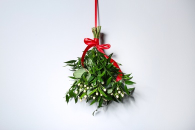 Mistletoe bunch with red bow hanging on light wall. Traditional Christmas decor