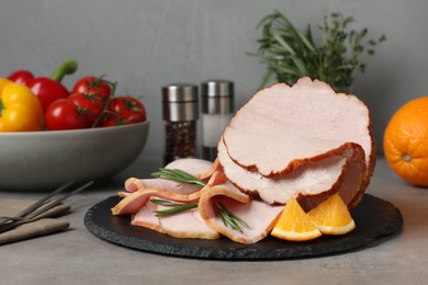 Photo of Delicious cut ham with rosemary and orange slices on grey table