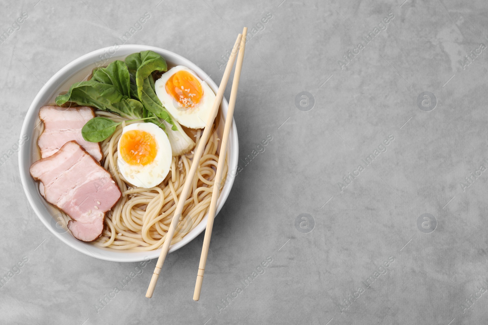 Photo of Delicious ramen with meat on light grey table, top view and space for text. Noodle soup
