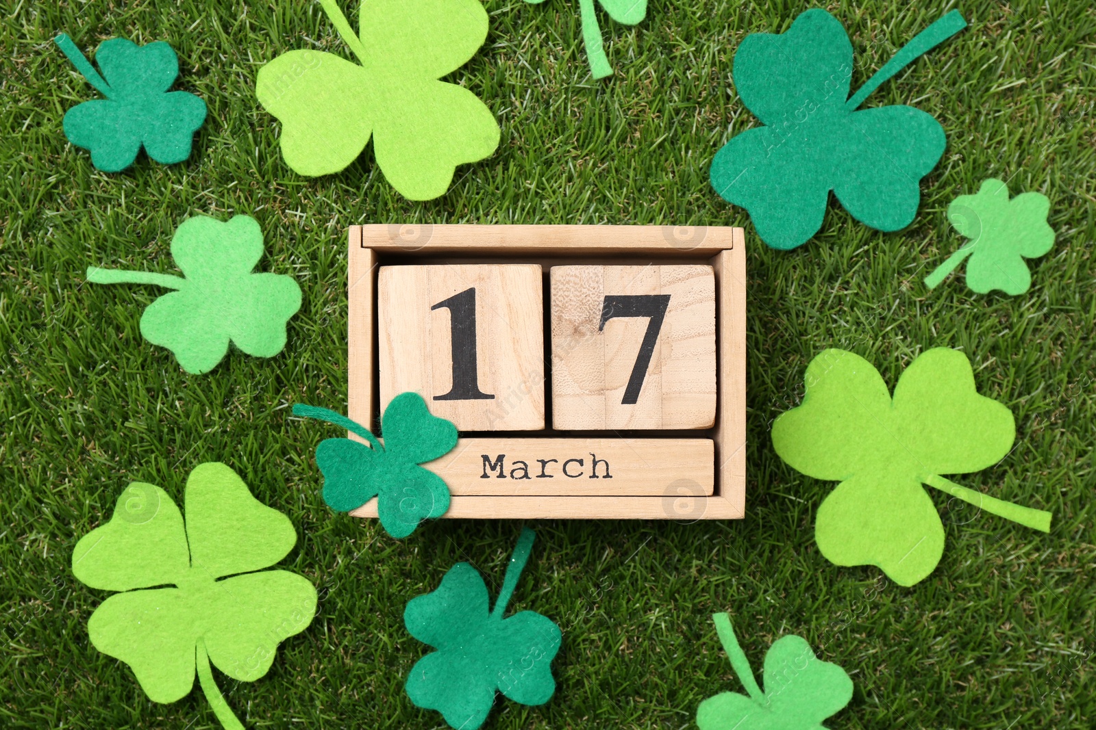 Photo of St. Patrick's day - 17th of March. Wooden block calendar and felt clover leaves on green grass, flat lay