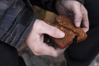 Photo of Poor homeless man holding piece of bread outdoors, closeup