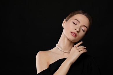 Photo of Young woman wearing elegant pearl jewelry on black background, space for text