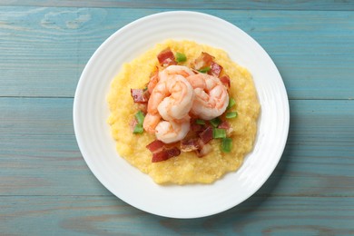 Photo of Plate with fresh tasty shrimps, bacon and grits on light blue wooden table, top view
