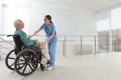 Nurse covering senior man in wheelchair with plaid at hospital. Medical assisting