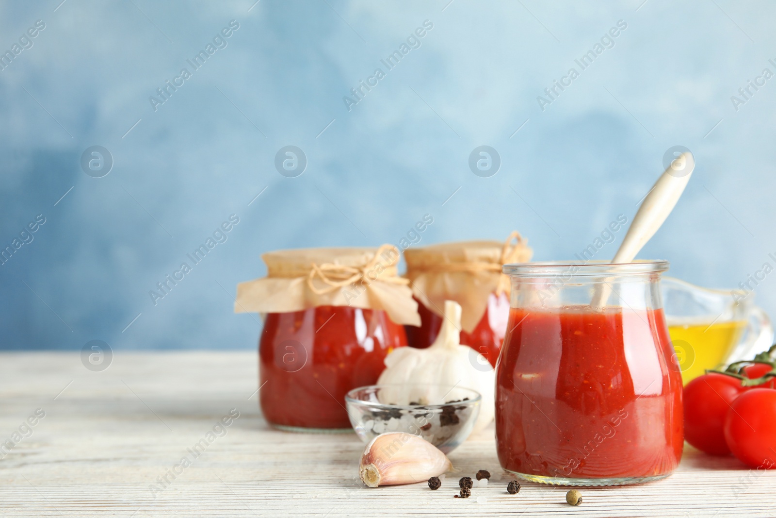 Photo of Composition with tomato sauce, spices and vegetables on table against color background. Space for text