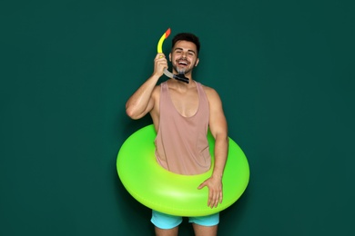 Photo of Funny young man with bright inflatable ring on dark green background
