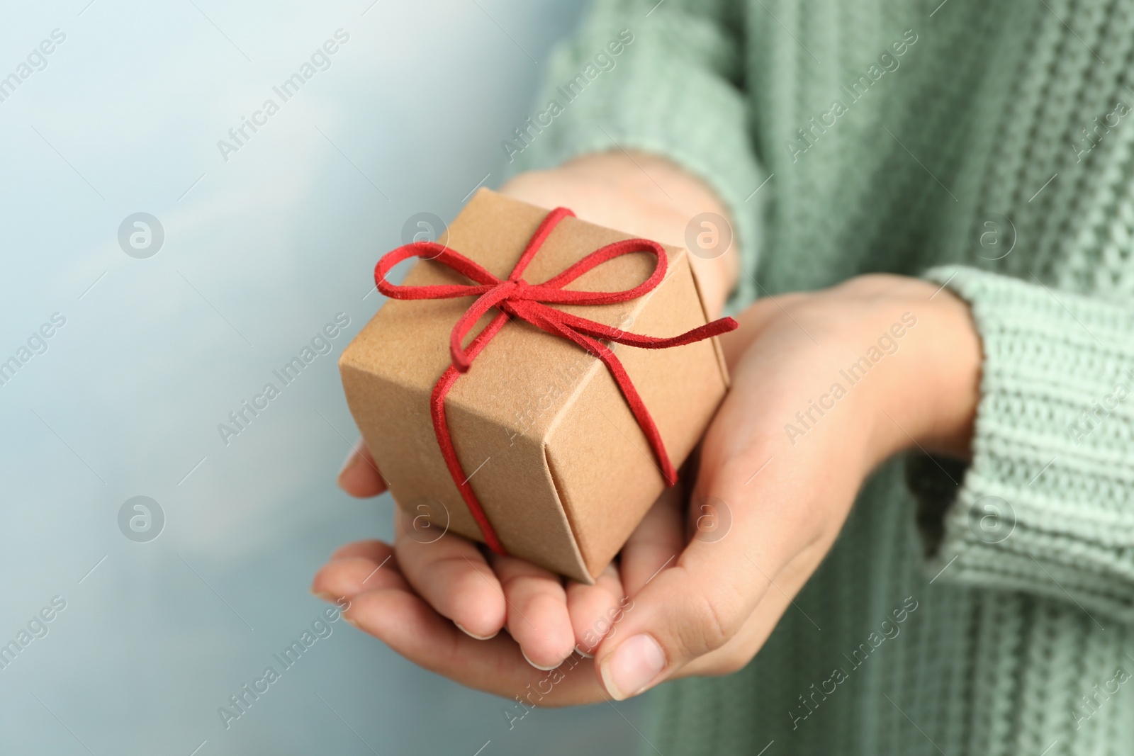 Photo of Woman holding beautiful Christmas gift on light blue background, closeup