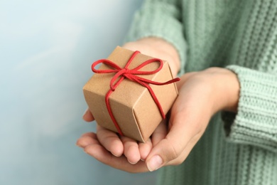 Photo of Woman holding beautiful Christmas gift on light blue background, closeup