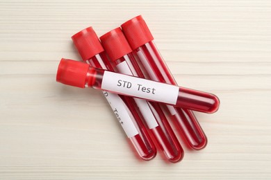 Photo of Tubes with blood samples and labels STD Test on white wooden table, flat lay