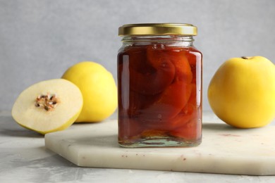Photo of Tasty homemade quince jam in jar and fruits on grey textured table, closeup