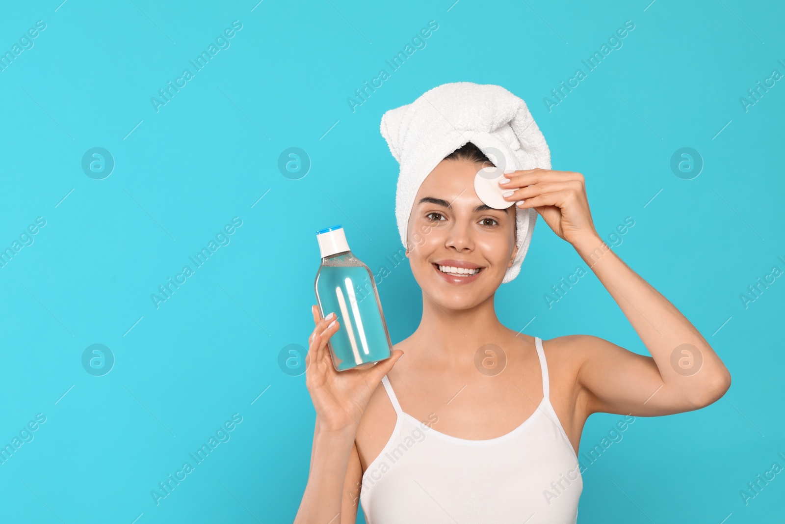 Photo of Young woman using cotton pad with micellar water on light blue background, space for text