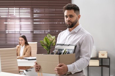 Photo of Upset dismissed man carrying box with personal stuff in office