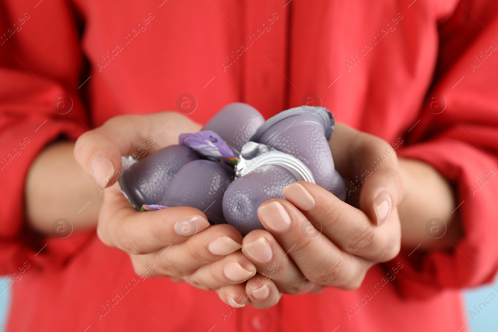 Photo of Woman holding many tasty bright jelly cups on light blue background, closeup