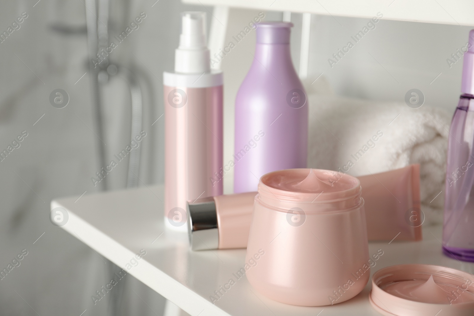 Photo of Different hair care products and towel on shelving unit in bathroom, closeup