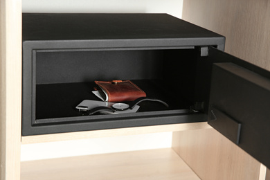 Open steel safe with wallet, watch and smartphone in wooden closet at hotel