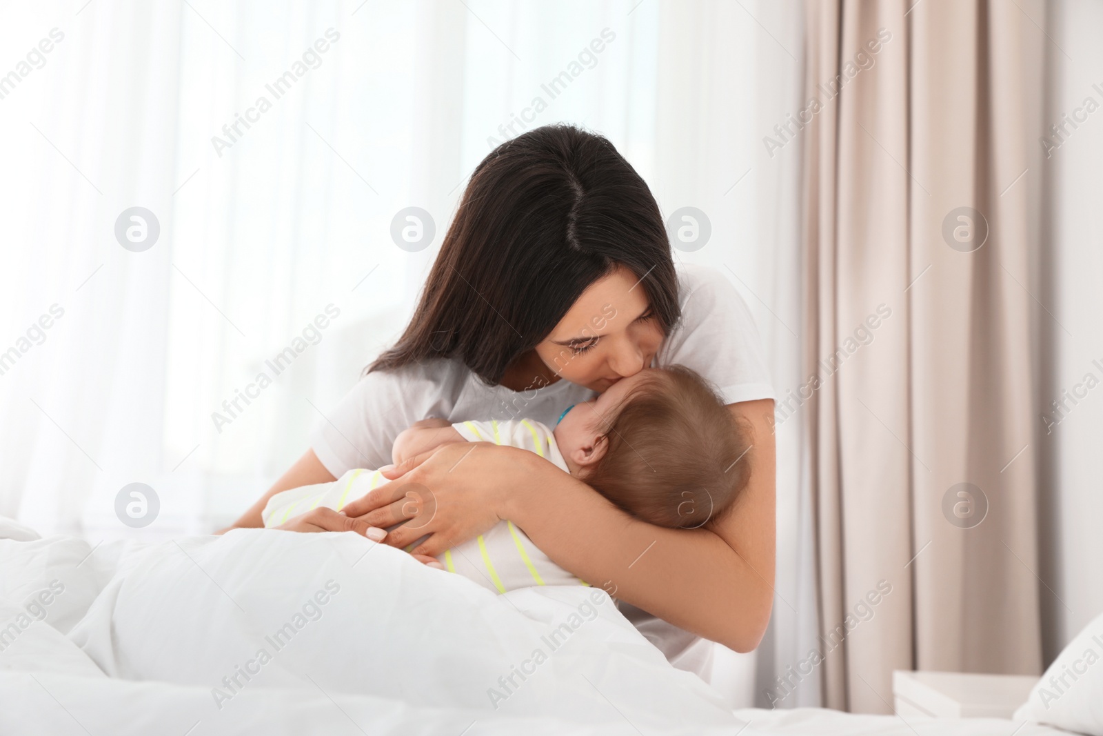 Photo of Mother with her adorable baby sitting on bed indoors