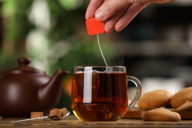 Photo of Man taking tea bag out of cup with beverage at wooden table, closeup