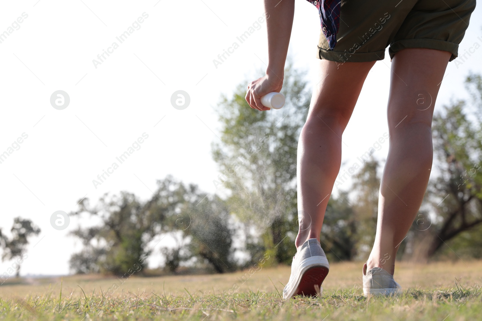 Photo of Woman applying insect repellent onto leg in park, closeup. Space for text