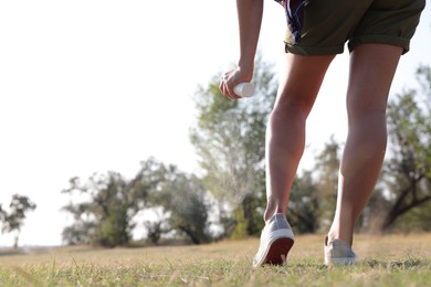 Woman applying insect repellent onto leg in park, closeup. Space for text