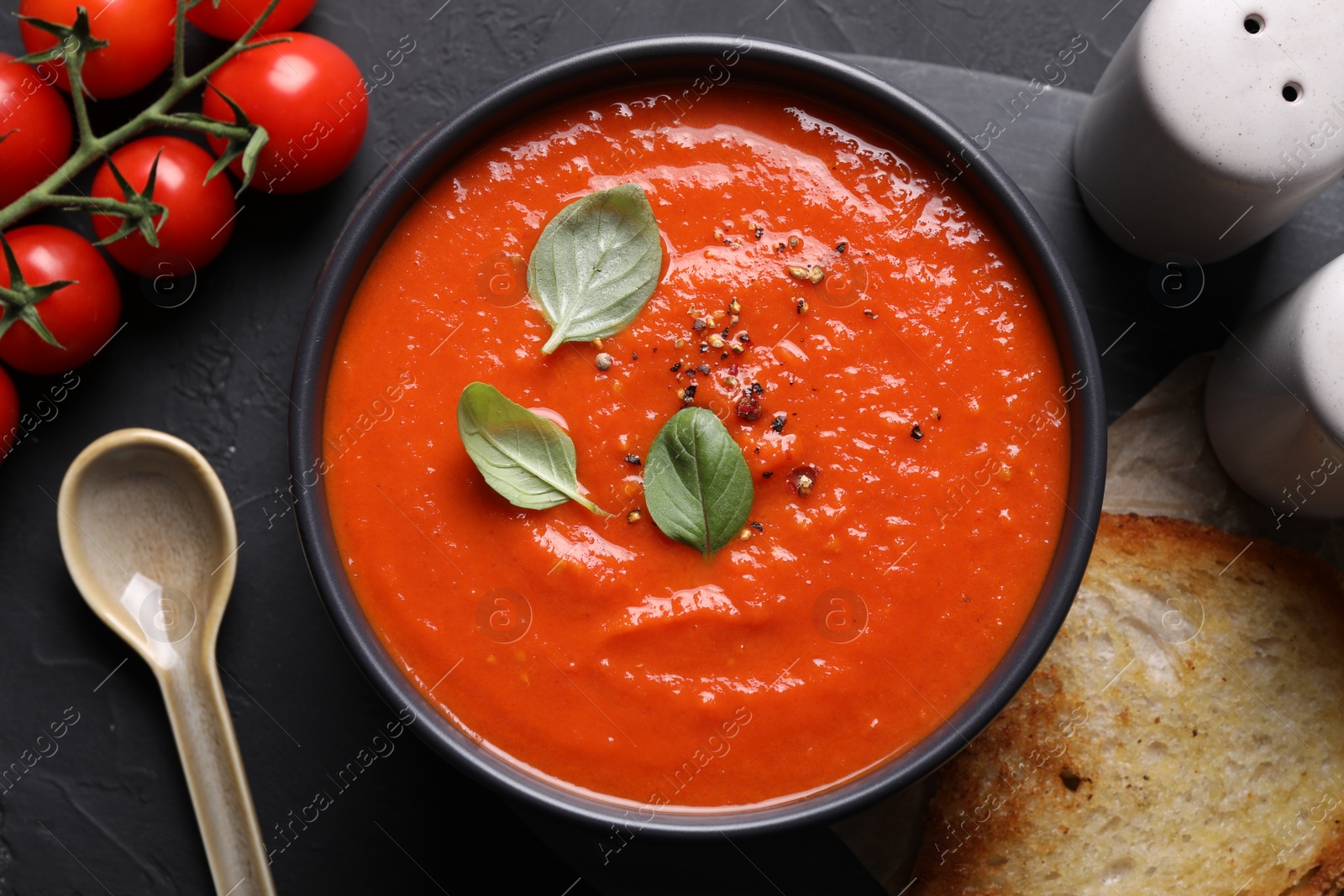 Photo of Delicious tomato cream soup served on black textured table, flat lay