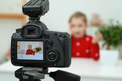 Photo of Cute little blogger with plant recording video at home, focus on camera