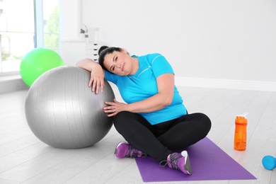 Overweight woman sitting on mat in gym