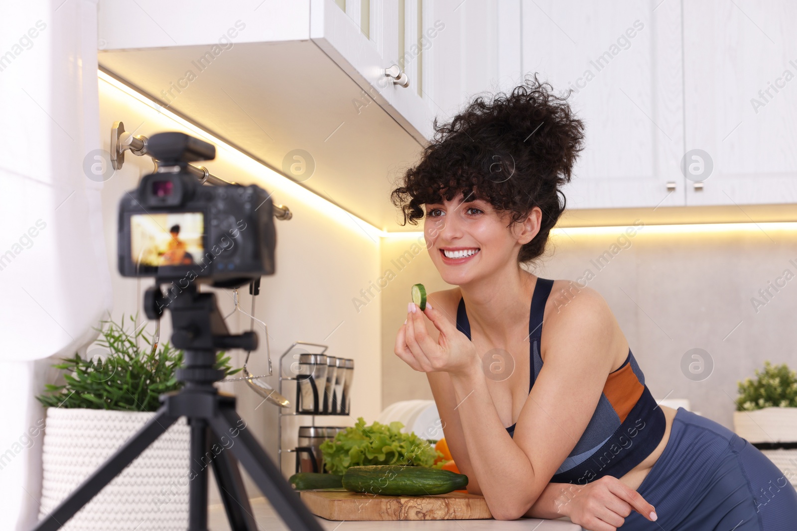 Photo of Smiling food blogger explaining something while recording video in kitchen