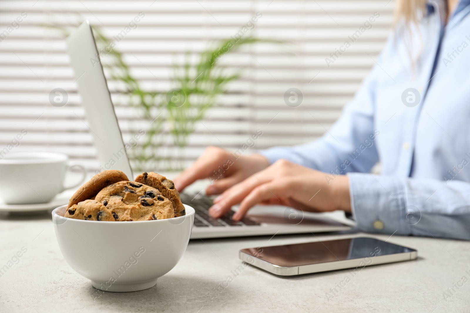 Photo of Office worker with laptop and chocolate chip cookies at light gray table, closeup